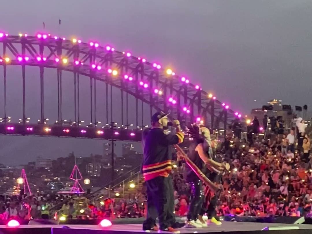 Performers on stage, the Harbour Bridge lit purple behind